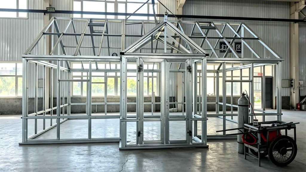 Front gable steel frame of Canadian greenhouse with screen door opening, assembled in workshop.